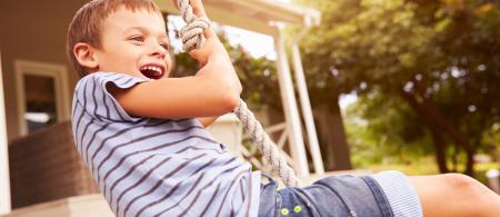 A child in a striped shirt laughs while playing on a rope swing