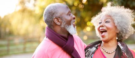 African American senior couple standing outside laughing together.