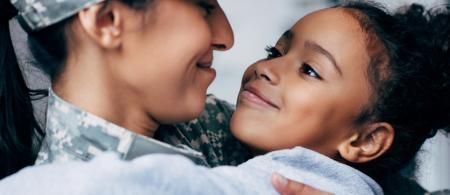 military mom and young daughter smiling at each other while they embrace