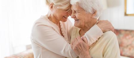 Elderly woman and daughter smiling and embracing with foreheads touching.
