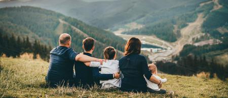 Parents and three children sitting on hillside looking into a river valley