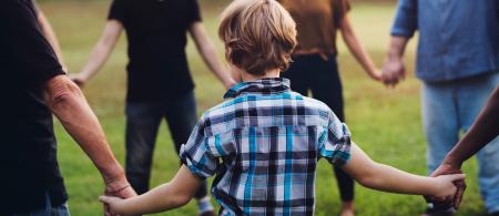 Child holding hands in a circle with a group of adults in a grassy park