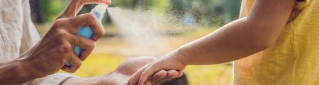 mother spraying son with mosquito repellent