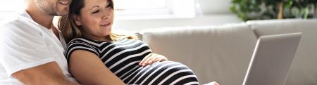 Pregnant woman and husband using laptop on a couch together