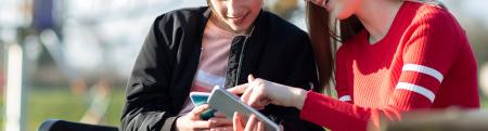 Teen girl with wheelchair looks at smart phone with friend