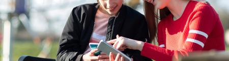 Teen girl with wheelchair looks at smart phone with friend