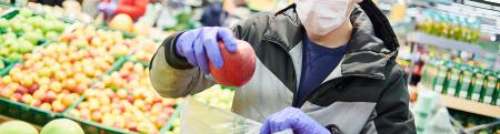 Man wearing cloth face covering and gloves shops for apples