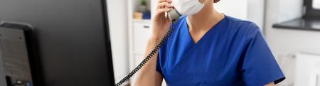 Woman wearing surgical mask speaks on phone and uses a computer