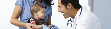 A woman holds her baby who is being examined by a doctor