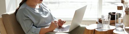 A woman wears headphones and works on a laptop computer