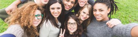 diverse group of youth with their arms around each other in a huddle looking at camera and smiling.