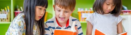 group of three young diverse children reading books with orange covers.