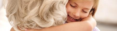 Affectionate grandmother and granddaughter are hugging. Little girl is smiling with eyes closed