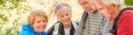 Two elderly couples looking at a map in a hiking area.