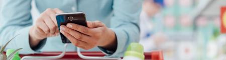 Person leaning on shopping cart and checking cellphone in supermarket