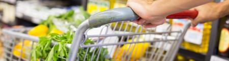 Hands pushing a shopping cart full of vegetables through a supermarket