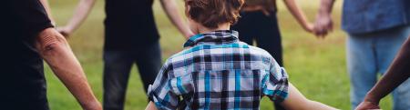Child holding hands in a circle with a group of adults in a grassy park