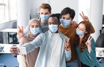 Diverse group of young adults wearing surgical masks takes a selfie with a camera phone