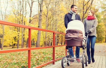 Young couple pushes a baby carriage through a park in fall
