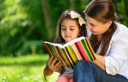Woman and young daughter read a book in a park