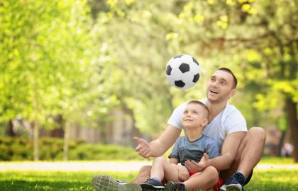 Man and young son play with soccer ball in a park