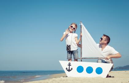 Girl and foster father playing with toy boat on a beach