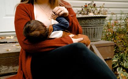 A woman sits outside breastfeeding an infant