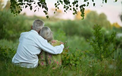 Older couple sitting under a tree in grassy field