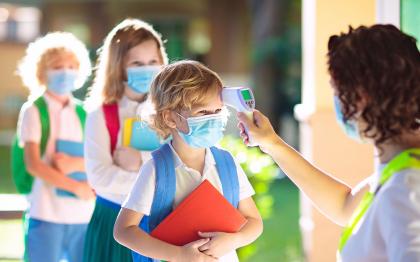 Child care provider taking temperature of masked child.