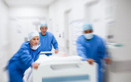 Emergency room workers wearing PPE push an empty hospital bed through a hallway