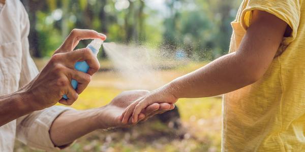 Parent spraying sanitizer or sunblock on child 