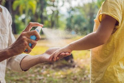 Parent spraying sanitizer or sunblock on child 