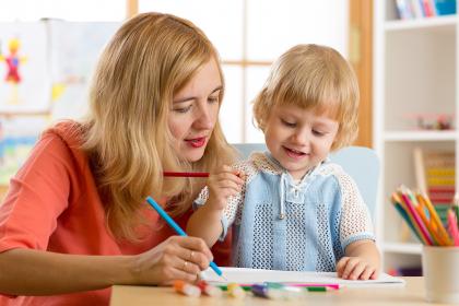 Childcare worker using colored pencils with toddler