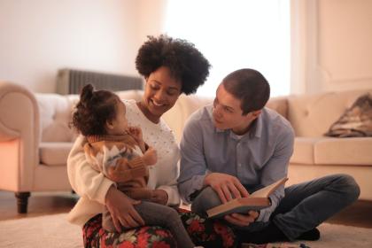 Two smiling adults reading with a toddler