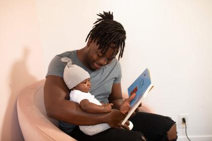 An adult sits in a chair reading to a baby