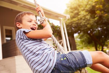 A child in a striped shirt laughs while playing on a rope swing