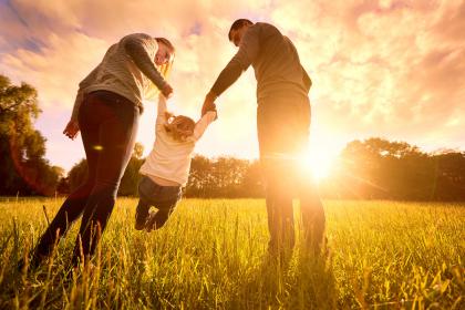 Two adults play with a toddler in a field near sunset
