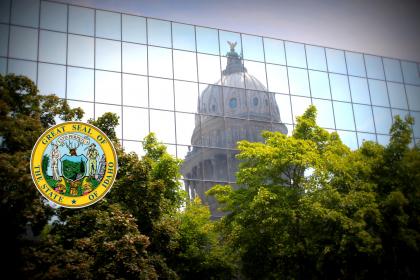 Hall of Mirrors Building reflects the Capitol Dome among trees with the Idaho State Seal.
