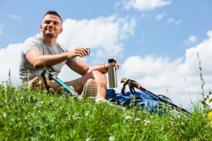 Young man with a prosthetic leg on a grassy knoll with his bicycle laying next to him.