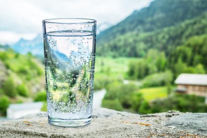 Frosty glass of water sitting on a stone blurring out forested mountain valley