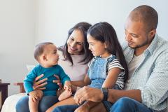 A mother and father sit with their daughter and baby