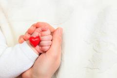 Parent and newborn hold small toy heart