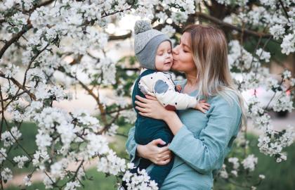 Mother holds young son in front of apple tree in blossom